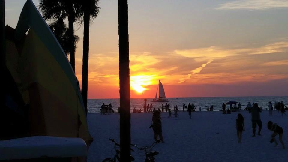 Gulf sunset, a sailboat in the Gulf, and people on the beach at Sunsets at Pier 60 in Clearwater Beach