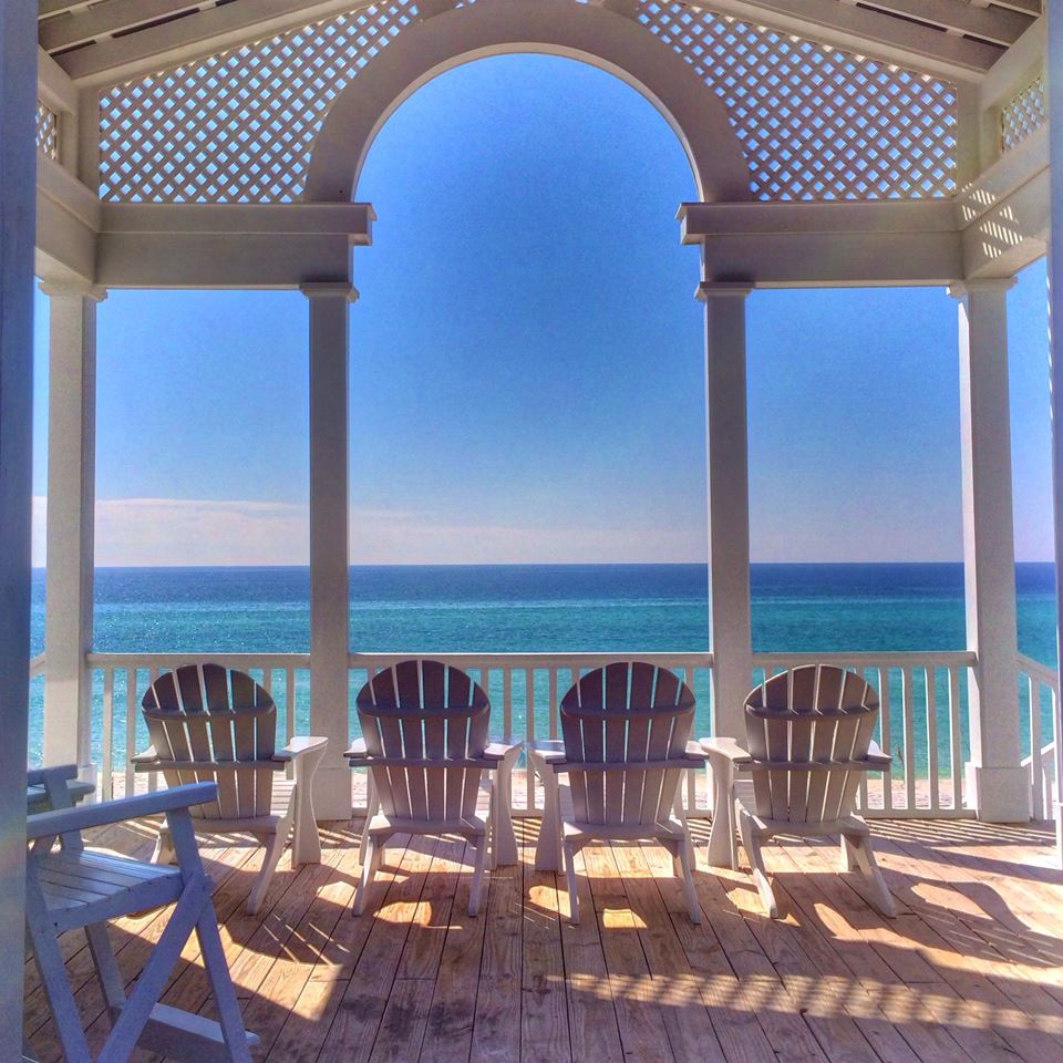 Columned and arched beachfront gazebo with four Adirondack chairs and a view of the Gulf