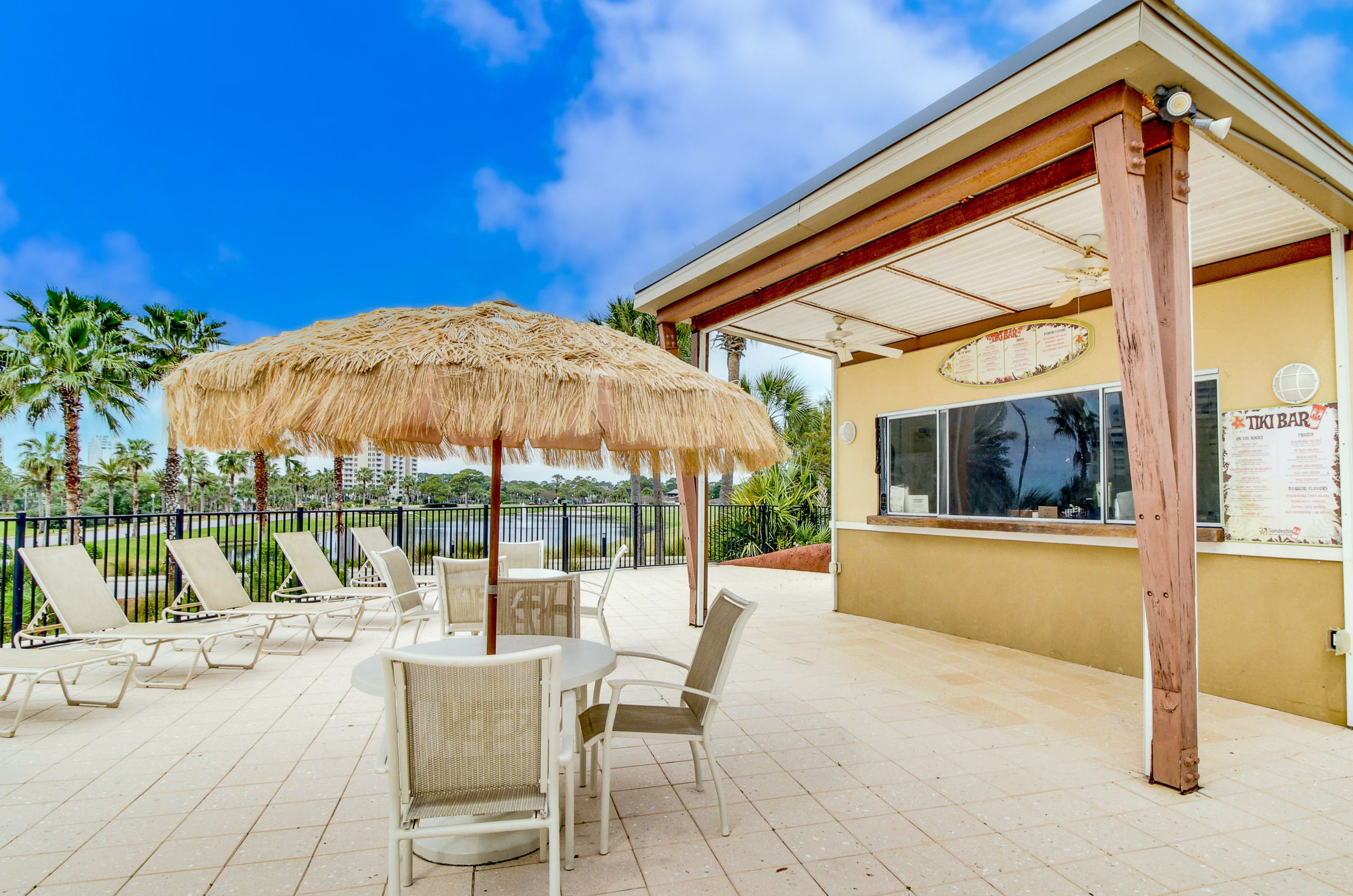 A poolside tiki hut bar with and patio seating and a lagoon featuring fountains nearby in the background