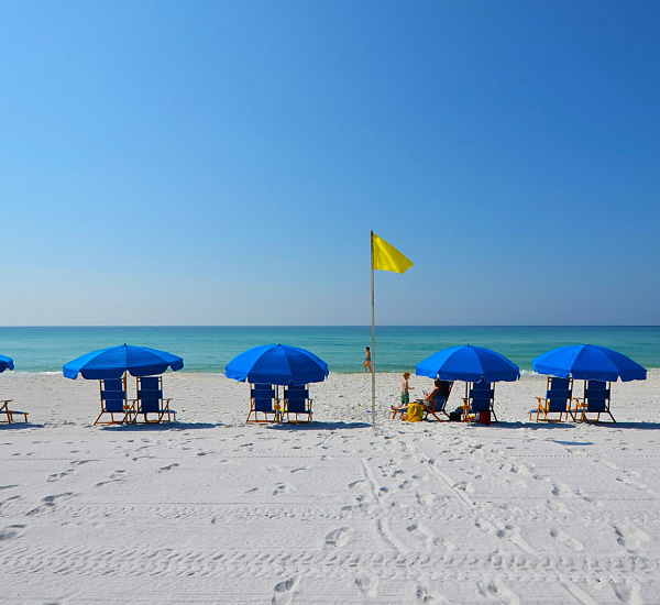 Blue umbrellas shade pairs of beach chairs on the sands at Island Princess Fort Walton.